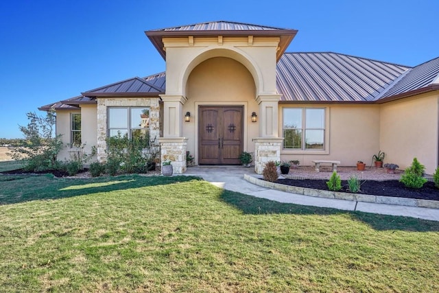 view of exterior entry featuring a standing seam roof, metal roof, a lawn, and stucco siding