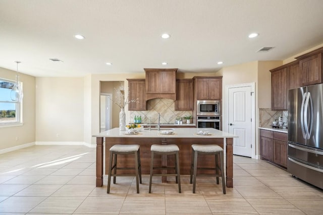 kitchen with appliances with stainless steel finishes, a center island with sink, tasteful backsplash, and a kitchen breakfast bar