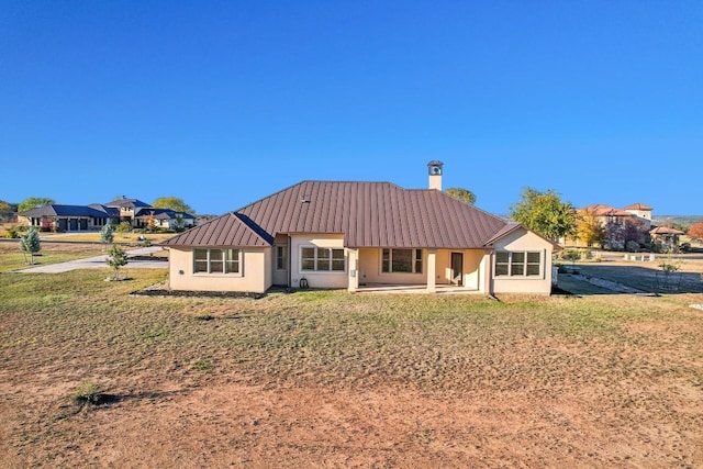 rear view of property with metal roof, stucco siding, and a lawn