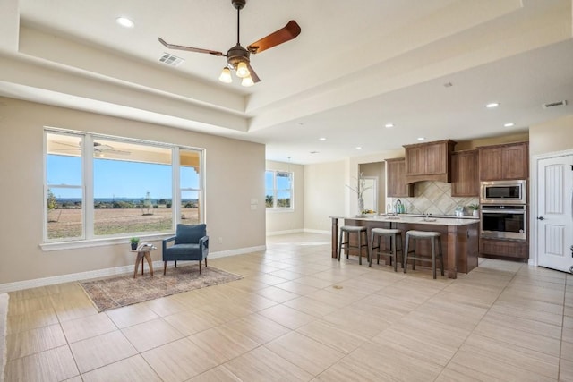 kitchen featuring decorative backsplash, a kitchen breakfast bar, stainless steel appliances, a kitchen island with sink, and ceiling fan