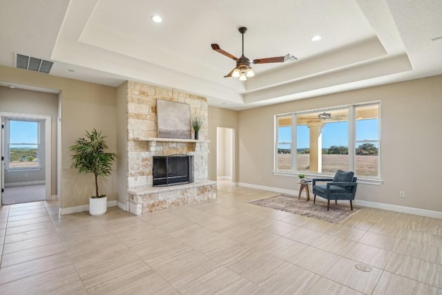 living room featuring a fireplace, a tray ceiling, and ceiling fan