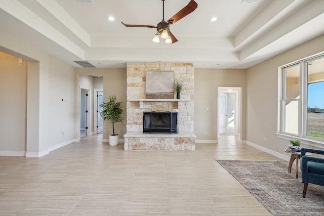 tiled living room with ceiling fan, a fireplace, and a tray ceiling