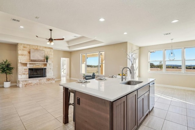 kitchen with a stone fireplace, a kitchen island with sink, sink, and hanging light fixtures