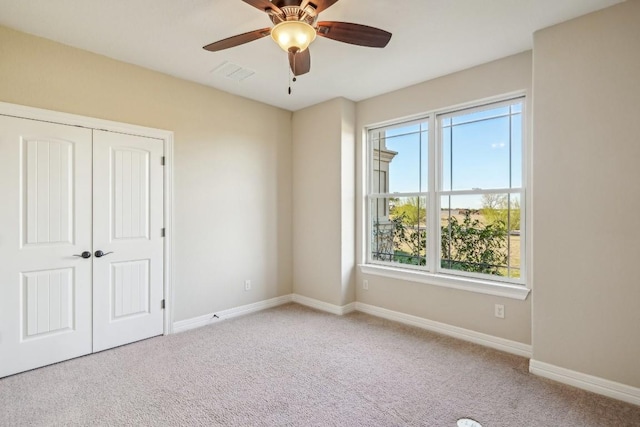 carpeted spare room with visible vents, baseboards, and a ceiling fan