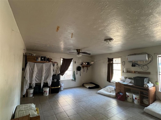 interior space with a wall mounted air conditioner, lofted ceiling, ceiling fan, light tile patterned floors, and a textured ceiling