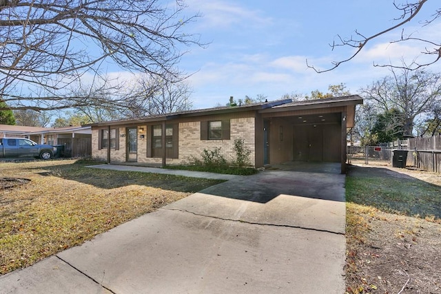 view of front of property with brick siding, concrete driveway, fence, a carport, and a front lawn