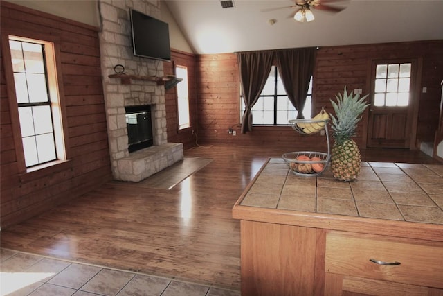 living room with a fireplace, wood walls, lofted ceiling, dark tile patterned floors, and ceiling fan