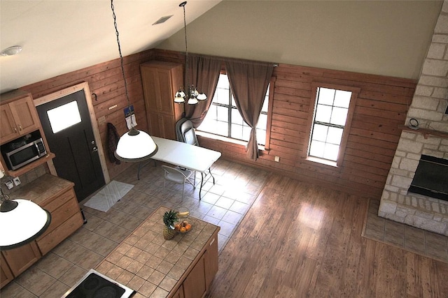 interior space featuring decorative light fixtures, wooden walls, tile countertops, and vaulted ceiling