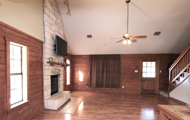 unfurnished living room with dark wood-type flooring, wood walls, high vaulted ceiling, ceiling fan, and a fireplace