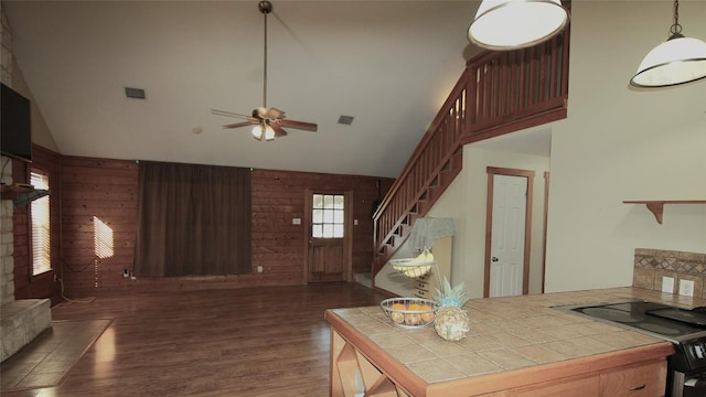 living room featuring a stone fireplace, dark wood-type flooring, wooden walls, and ceiling fan