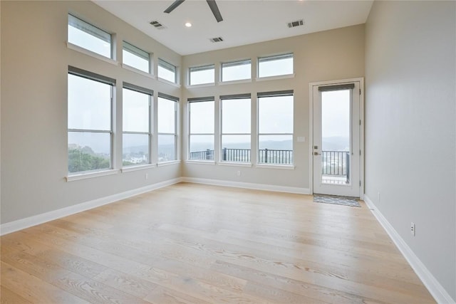 empty room featuring ceiling fan, a healthy amount of sunlight, a high ceiling, and light wood-type flooring