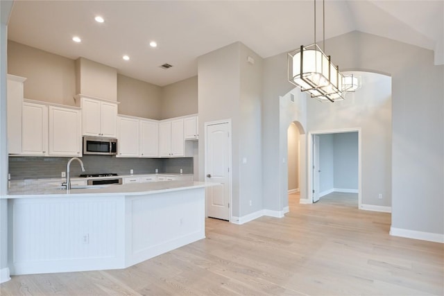 kitchen featuring white cabinets, stainless steel appliances, high vaulted ceiling, and light hardwood / wood-style flooring