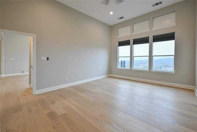 unfurnished room featuring a towering ceiling, light hardwood / wood-style floors, and ceiling fan