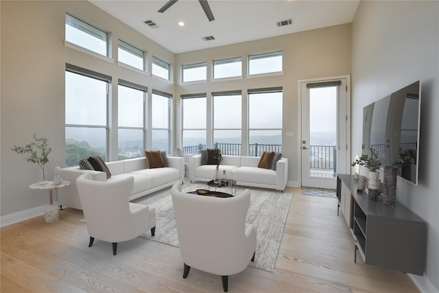 living room featuring a towering ceiling, light hardwood / wood-style floors, a wealth of natural light, and ceiling fan