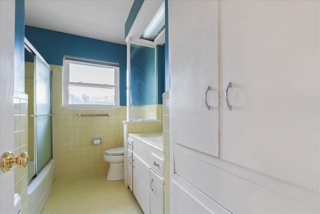 full bathroom with tile patterned floors, bath / shower combo with glass door, vanity, tile walls, and toilet