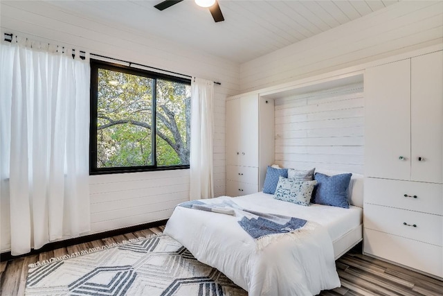 bedroom with dark hardwood / wood-style floors, ceiling fan, and wooden walls