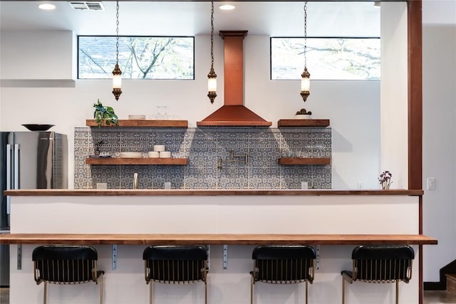 interior space featuring stainless steel refrigerator, wall chimney exhaust hood, and decorative light fixtures