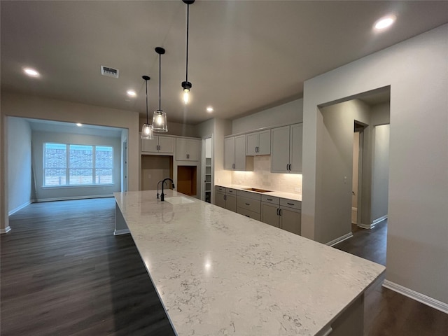 kitchen with light stone countertops, sink, hanging light fixtures, and a large island with sink