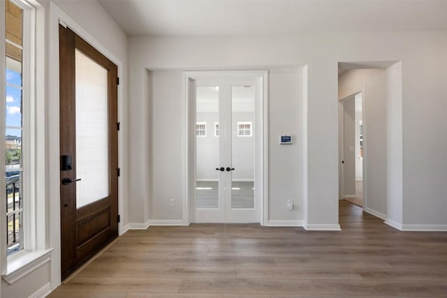 foyer entrance with light wood-style floors, french doors, and baseboards