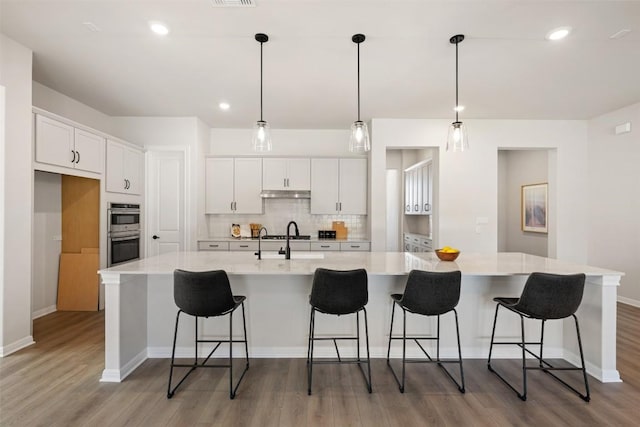 kitchen featuring backsplash, double oven, white cabinetry, a sink, and light wood-type flooring