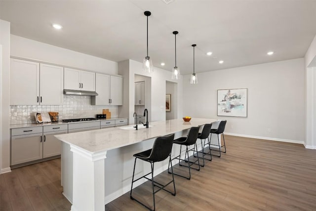 kitchen featuring black gas stovetop, under cabinet range hood, a sink, backsplash, and light wood finished floors