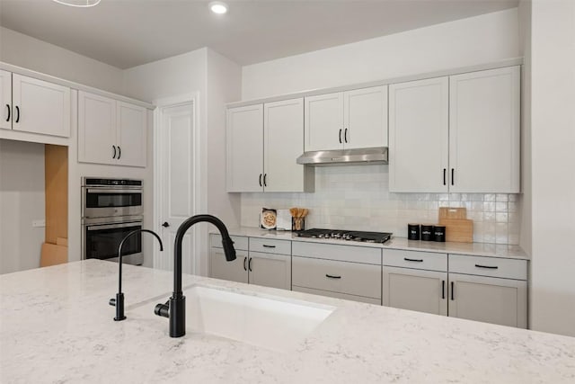 kitchen with stainless steel appliances, decorative backsplash, white cabinetry, a sink, and under cabinet range hood