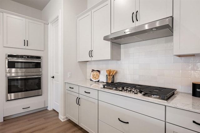 kitchen with decorative backsplash, light wood-style floors, appliances with stainless steel finishes, under cabinet range hood, and white cabinetry