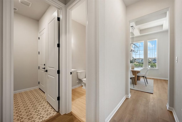 hallway featuring light wood-style floors, a chandelier, visible vents, and baseboards