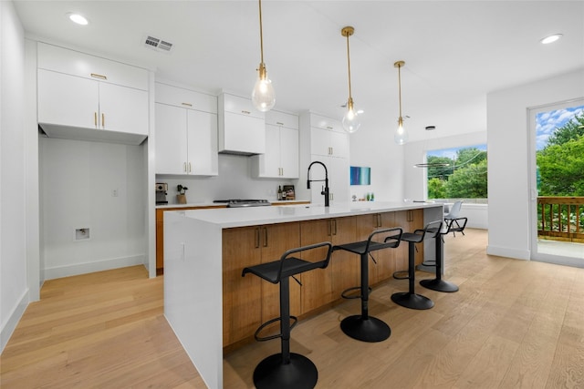 kitchen with a center island with sink, white cabinets, pendant lighting, and light wood-type flooring