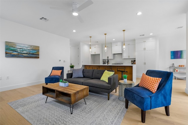 living room featuring ceiling fan, light hardwood / wood-style floors, and sink