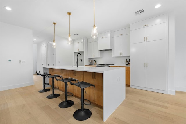 kitchen with sink, pendant lighting, white cabinets, light hardwood / wood-style floors, and an island with sink