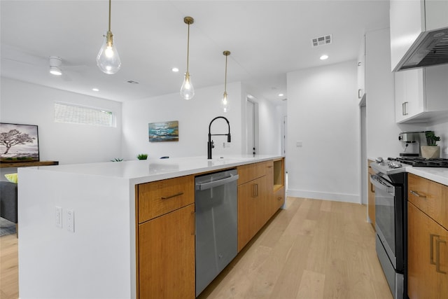 kitchen with white cabinets, wall chimney range hood, a large island, light hardwood / wood-style floors, and stainless steel appliances