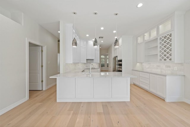 kitchen with kitchen peninsula, light wood-type flooring, backsplash, pendant lighting, and white cabinetry