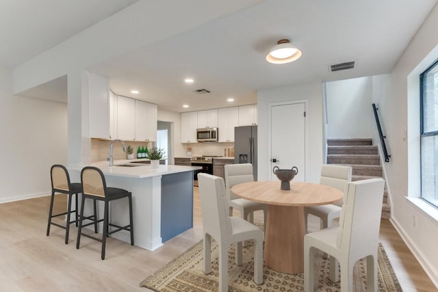 kitchen featuring kitchen peninsula, stainless steel appliances, light wood-type flooring, white cabinets, and sink