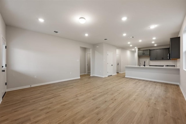 727 Palo Brea Loop, Hutto, TX 78634 - unfurnished living room featuring light wood-style floors, baseboards, recessed lighting, and a sink