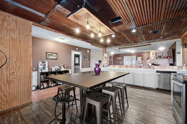 kitchen with appliances with stainless steel finishes, hardwood / wood-style flooring, white cabinetry, and a kitchen breakfast bar