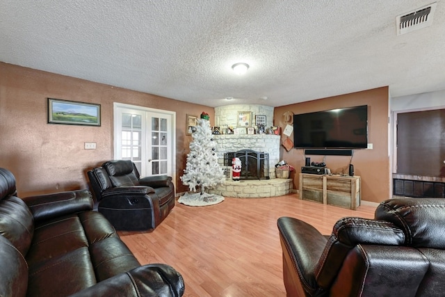 living room featuring hardwood / wood-style floors, a textured ceiling, a stone fireplace, and french doors