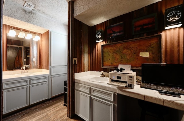 bathroom with a textured ceiling, hardwood / wood-style flooring, wooden walls, and sink