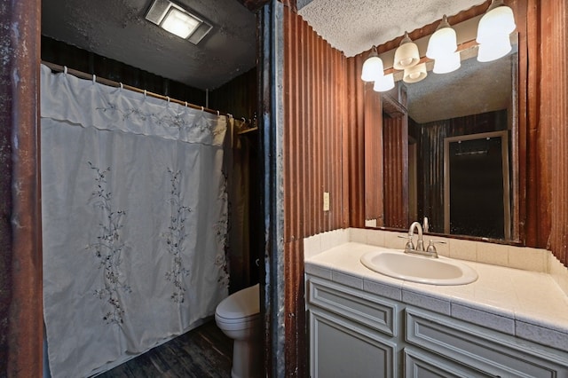 bathroom featuring vanity, wood walls, toilet, and a textured ceiling