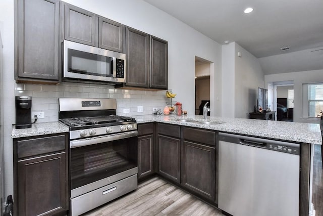 kitchen featuring stainless steel appliances, kitchen peninsula, sink, and decorative backsplash