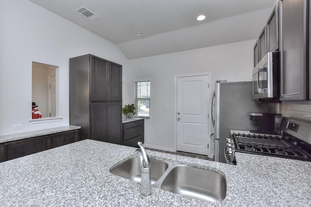 kitchen with sink, stainless steel appliances, light stone counters, dark brown cabinetry, and vaulted ceiling