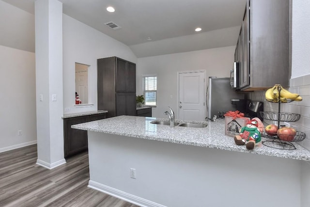 kitchen featuring dark brown cabinets, kitchen peninsula, sink, and light stone countertops