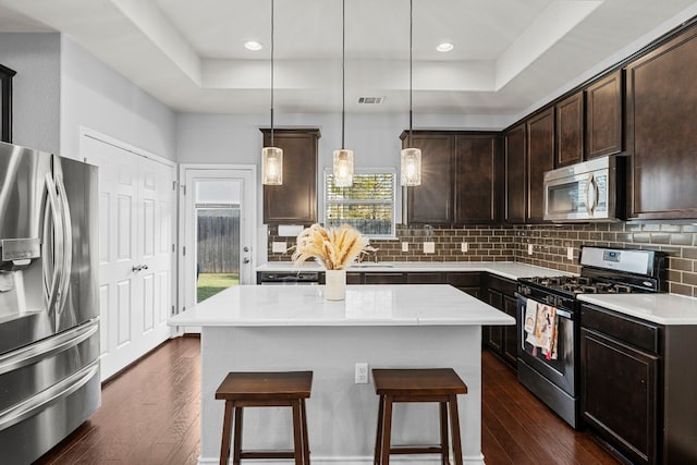 kitchen featuring decorative light fixtures, a tray ceiling, decorative backsplash, a kitchen island, and appliances with stainless steel finishes