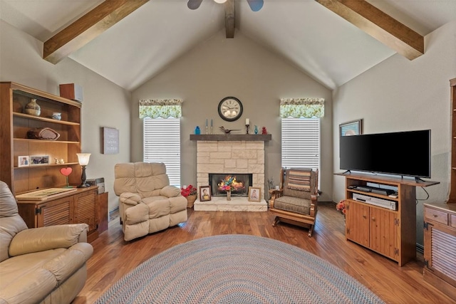 living room featuring lofted ceiling with beams, a stone fireplace, and wood-type flooring