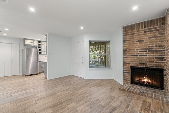 unfurnished living room featuring a brick fireplace and light wood-type flooring