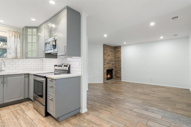 kitchen with sink, gray cabinets, light wood-type flooring, a fireplace, and appliances with stainless steel finishes