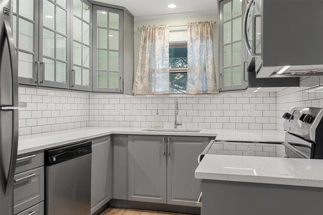 kitchen with light stone countertops, decorative backsplash, stainless steel appliances, sink, and gray cabinets