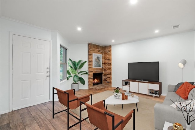 living room featuring a brick fireplace, ornamental molding, and light wood-type flooring