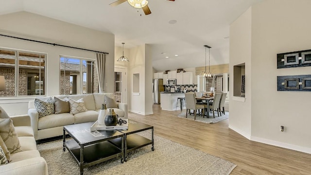 living room with vaulted ceiling, light hardwood / wood-style flooring, and ceiling fan with notable chandelier