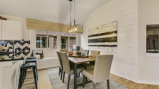 dining room featuring light hardwood / wood-style floors, lofted ceiling, sink, and a chandelier